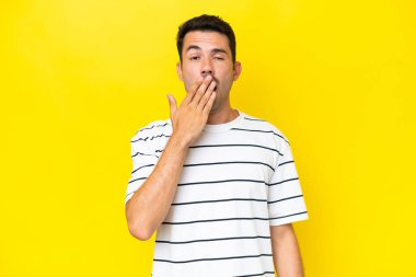 Izole sarı arka plan esneme üzerinde genç yakışıklı adam esneme ve el ile geniş açık ağız kapsayan