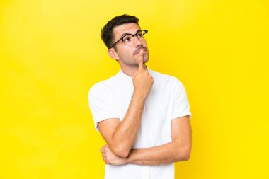 Soyutlanmış sarı arka planda genç yakışıklı bir adamın yukarı bakarken şüpheleri var.