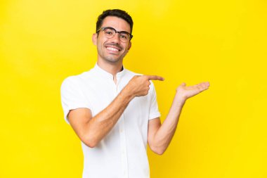 İzole edilmiş sarı arka planda genç yakışıklı bir adam. Avucunun içinde hayali bir ilan tutuyor.