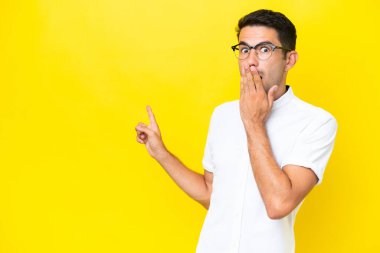 Soyutlanmış sarı arka planda genç yakışıklı bir adam sürpriz bir ifadeyle işaret ederken
