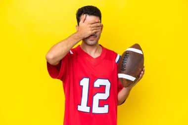 İzole edilmiş sarı arka planda ragbi oynayan yakışıklı genç bir adam elleriyle gözlerini kapatıyor. Bir şey görmek istemiyorum.