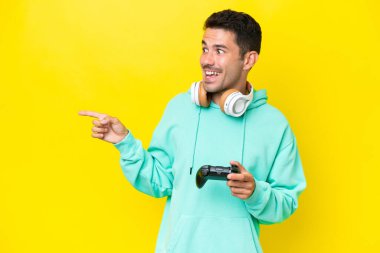 Genç yakışıklı bir adam, izole edilmiş duvarın üzerinde video oyunu kontrolörüyle oynuyor. Parmakla göstererek bir ürün sunuyor.
