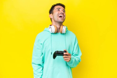 Bir video oyunu kontrolörüyle oynayan yakışıklı genç adam izole duvarın üstünde gülüyor.