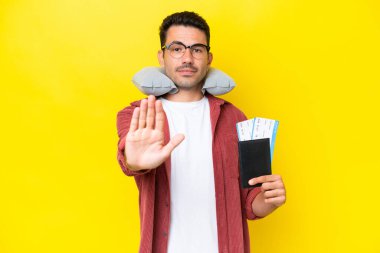 Şişirilebilir Seyahat Yastığı ile genç yakışıklı adam izole edilmiş sarı arka plan üzerinde durma hareketi yapıyor.