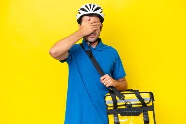 Termal sırt çantalı yakışıklı genç bir adam izole edilmiş sarı arka planda gözlerini elleriyle kapatıyor. Bir şey görmek istemiyorum.