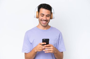 Soyutlanmış beyaz arka planda genç yakışıklı bir adam müzik dinliyor ve cep telefonu arıyor.