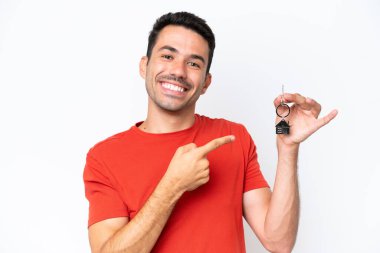Evin anahtarlarını tutan yakışıklı genç adam izole edilmiş beyaz arka planda ve onu işaret ediyor.