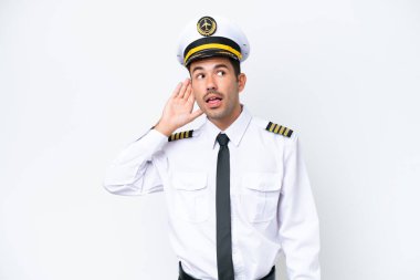 İzole edilmiş beyaz arka plan üzerinde uçak pilotu. Kulağına elini koyarak bir şey dinliyor.