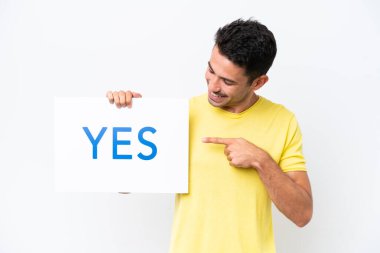 İzole edilmiş beyaz arka planda genç yakışıklı bir adam elinde bir pankart tutuyor. Evet diyor ve işaret ediyor.