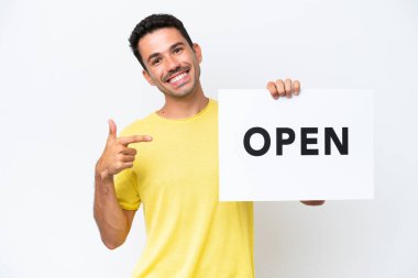İzole edilmiş beyaz arka planda genç yakışıklı bir adam elinde açık yazılı bir pankart tutuyor ve onu işaret ediyor.