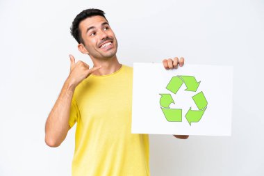 İzole edilmiş beyaz arka plan üzerinde genç yakışıklı bir adam elinde geri dönüşüm simgesiyle bir pankart tutuyor ve telefon hareketi yapıyor.