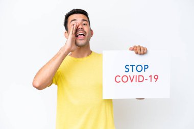 Beyaz arka plan üzerinde genç yakışıklı bir adam elinde yazılı bir levhayla Covid 19 'u durdurun ve bağırın