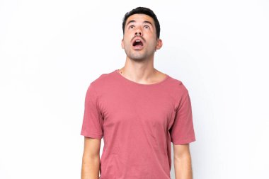 Soyutlanmış beyaz arka planda genç yakışıklı bir adam yukarı bakıyor ve şaşırmış bir ifadeyle