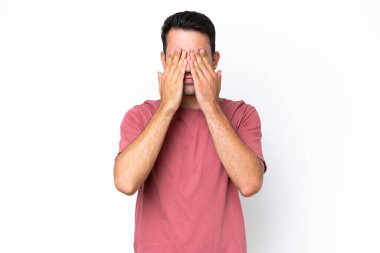 İzole edilmiş beyaz arka planda genç yakışıklı adam gözlerini elleriyle kapatıyor.
