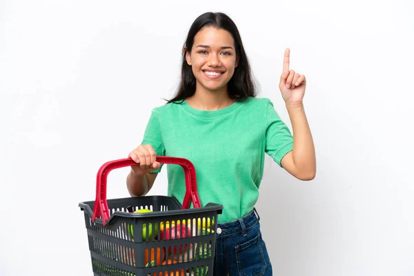 一个年轻的哥伦比亚女人拿着一篮子被白色背景隔离的食物 展示并举起一个手指表示她是最棒的 — 图库照片