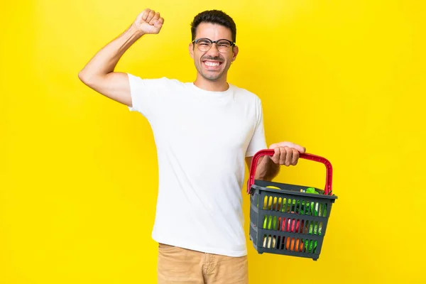 Mladý Pohledný Muž Drží Nákupní Košík Plný Potravin Přes Izolované — Stock fotografie