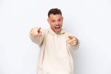 Beyaz arka planda izole edilmiş beyaz, yakışıklı genç adam şaşırmış ve ön tarafı işaret ediyor.