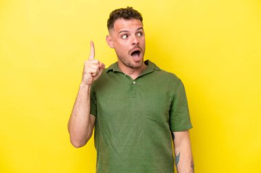 Sarı arka planda izole genç beyaz yakışıklı adam çözümü bulmak için parmağını kaldırıyor.
