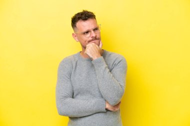 Beyaz tenli yakışıklı adam sarı arka planda izole edilmiş. Şüpheleri ve düşünceleri var.