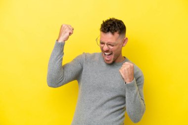Sarı arka planda izole edilmiş beyaz yakışıklı bir adam zaferi kutluyor.