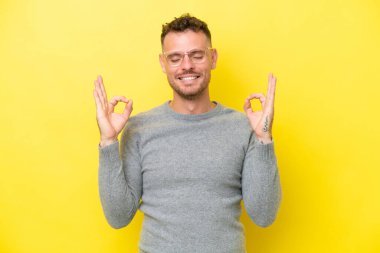 Zen pozisyonunda sarı arka planda izole genç beyaz yakışıklı adam.