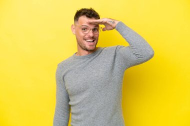 Beyaz tenli yakışıklı adam sarı arka planda izole edilmiş. Bir şeye bakmak için uzaklara bakıyor.