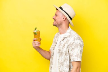 Sarı arka planda izole edilmiş bir kokteyl tutan beyaz bir adam yan yana gülüyor.