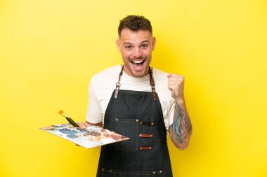 Sarı arka planda izole edilmiş palet tutan beyaz bir adam zaferi kutluyor.