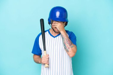 Kasklı ve yarasalı beyzbol oyuncusu yorgun ve hasta bir ifadeyle mavi arka planda izole edildi