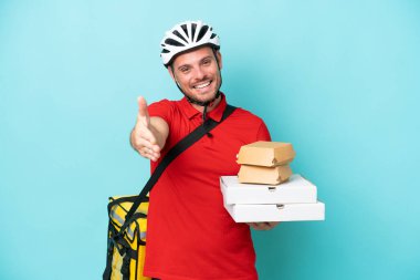 Termal sırt çantalı, fast food taşıyan, mavi arka planda izole edilmiş beyaz bir adam iyi bir anlaşma için el sıkışıyor.