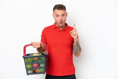 Beyaz arka planda izole edilmiş yiyecek dolu bir sepet taşıyan genç beyaz bir adam çözümü fark ederken parmağını kaldırmayı amaçlıyordu.