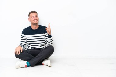 Yerde oturan genç adam beyaz arka planda izole edilmiş yukarı bakıyor ve şaşırıyor.