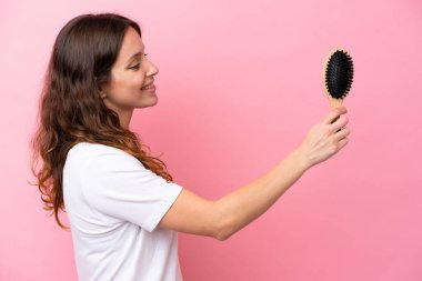 Pembe arka planda saçı taranmış, mutlu bir ifadeyle genç, beyaz bir kadın.