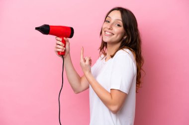 Pembe arka planda izole edilmiş bir saç kurutma makinesi tutan beyaz bir kadın.