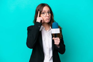 Genç TV sunucusu kadın mavi arka planda izole edilmiş bir fikir düşünüyor.