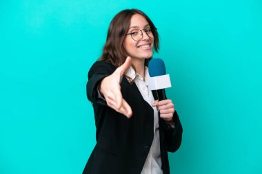 Genç TV sunucusu kadın mavi arka planda izole edilmiş, iyi bir anlaşma için el sıkışıyor.
