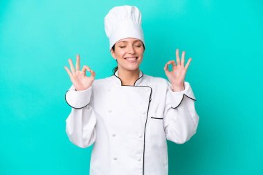 Beyaz tenli genç aşçı kadın Zen pozunda mavi arka planda izole edilmiş.