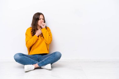 Beyaz duvarda izole bir şekilde yerde oturan genç beyaz kadın öksürük ve kötü hissediyordu.