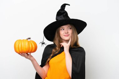 Genç ve güzel bir kadın kostümü, beyaz arka planda izole edilmiş bir balkabağı tutan cadı gibi yukarı bakarken bir fikir düşünüyor.