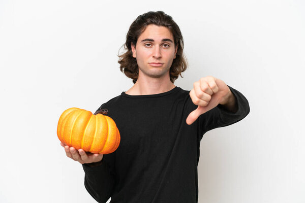 Young handsome man holding a pumpkin isolated on white background showing thumb down with negative expression