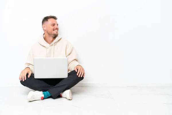 Jovem Caucasiano Com Laptop Sentado Chão Isolado Fundo Branco Olhando — Fotografia de Stock