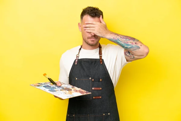 年轻的艺术家卡西亚人手拿着一个被黄色背景隔离的调色板 用手遮住眼睛 不想看到的东西 — 图库照片
