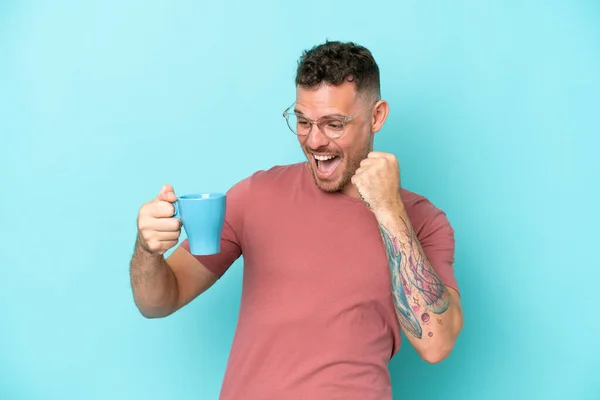 Młody Biały Mężczyzna Trzymając Filiżankę Kawy Odizolowany Niebieskim Tle Świętując — Zdjęcie stockowe