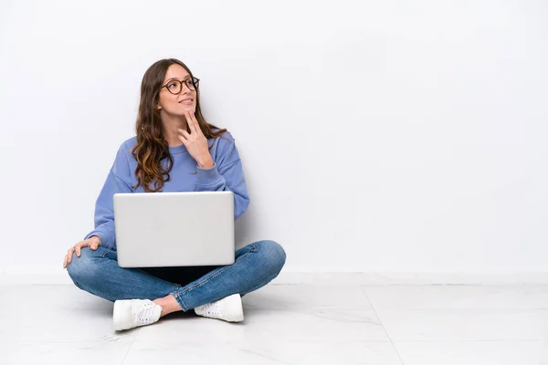 年轻的高加索女人 带着笔记本电脑坐在地板上 与白色背景隔离 抬起头微笑着 — 图库照片