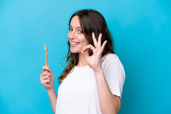 Young Caucasian Woman Brushing Teeth Isolated Blue Background Showing Sign — Zdjęcie stockowe
