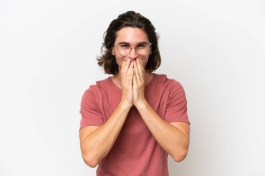 Genç ve yakışıklı bir adam beyaz arka planda izole edilmiş mutlu ve gülümseyen elleriyle ağzını kapatıyor.