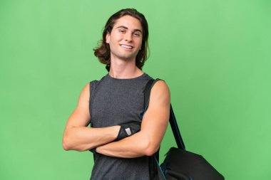 Genç sporcu yakışıklı adam yeşil renkli arka planda izole edilmiş, kolları bağlı ve ileriye bakıyor.