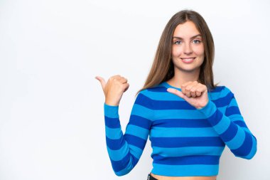 Beyaz arka planda izole edilmiş genç beyaz kadın bir ürünü sunmak için kenarı işaret ediyor.