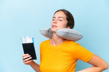 Şişirilebilir seyahat yastığı olan genç ve güzel bir kadın mavi arka planda izole edilmiş.