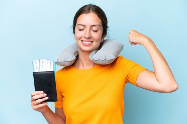 Şişirilebilir seyahat yastığı olan genç ve güzel bir kadın mavi arka planda izole edilmiş güçlü bir jest yapıyor.